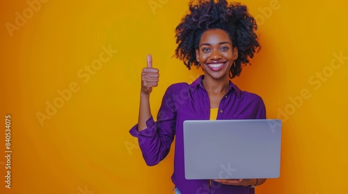 Portrait of a beautiful young lady holding her netbook thumb up while wearing an elegant violet garment on a yellow background photo