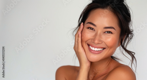 A portrait of a beautiful Asian woman with bright skin who has good health. She is smiling with confidence and a charming face while touching her well cared skin.