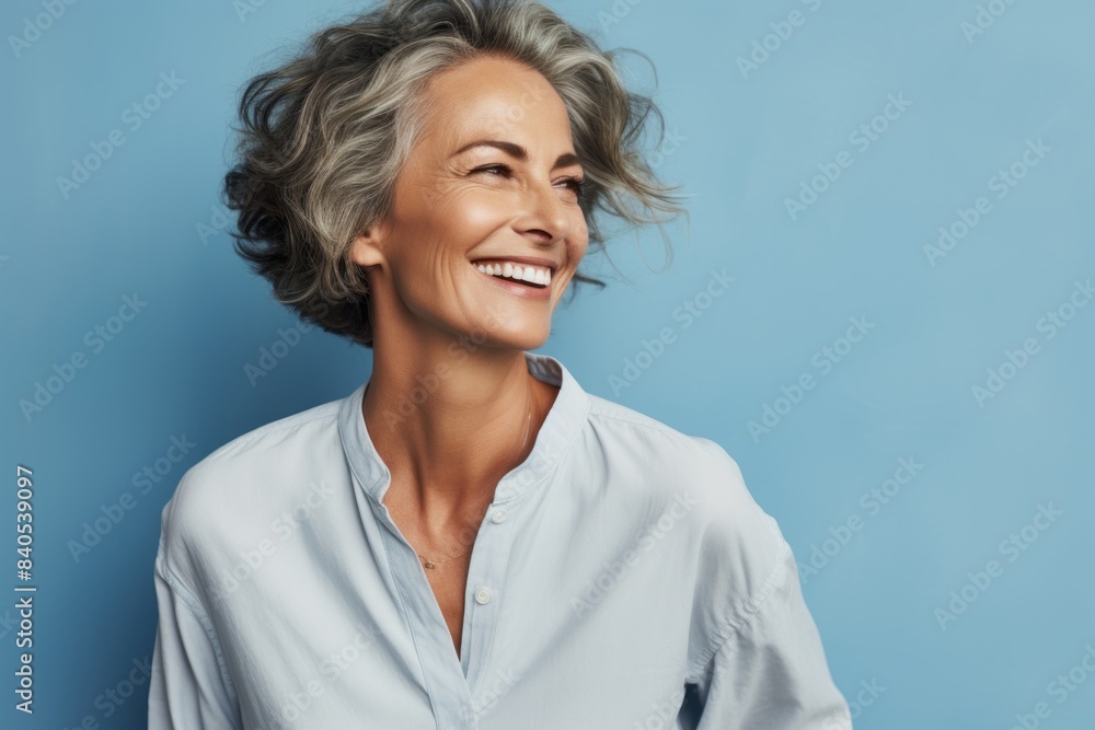 Portrait of a smiling woman in her 50s wearing a simple cotton shirt in front of pastel blue background Portrait of a smiling woman in her 50s wearing a simple cotton shirt in front of pastel blue background