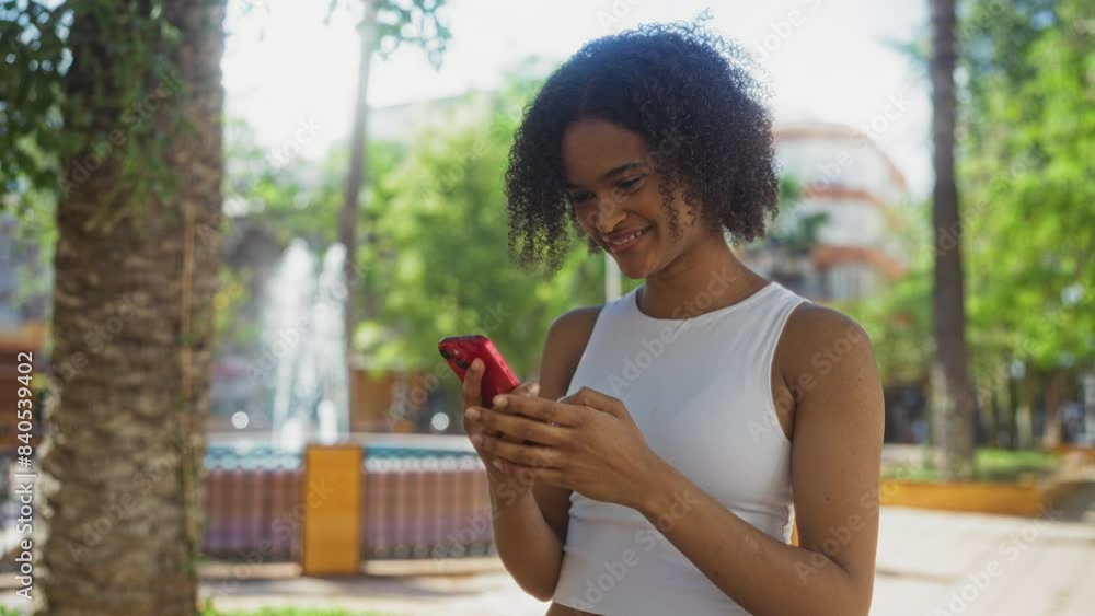 A beautiful young black woman with curly hair uses a smartphone in an urban park, creating a contrast of modern technology and natural surroundings with fountains and greenery. A beautiful young black woman with curly hair uses a smartphone in an urban park, creating a contrast of modern technology and natural surroundings with fountains and greenery.