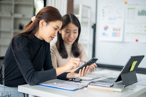 Two women are sitting at a desk looking at a cell phone