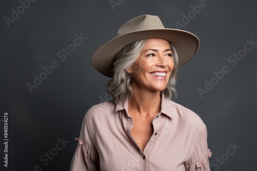 Portrait of a happy woman in her 50s wearing a rugged cowboy hat while standing against pastel gray background © CogniLens