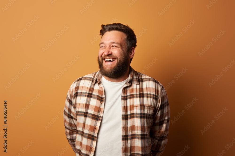 Portrait of a grinning man in his 30s wearing a comfy flannel shirt isolated in pastel brown background Portrait of a grinning man in his 30s wearing a comfy flannel shirt isolated in pastel brown background