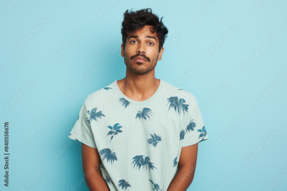Portrait of a glad indian man in his 20s donning a trendy cropped top while standing against soft blue background Portrait of a glad indian man in his 20s donning a trendy cropped top while standing against soft blue background