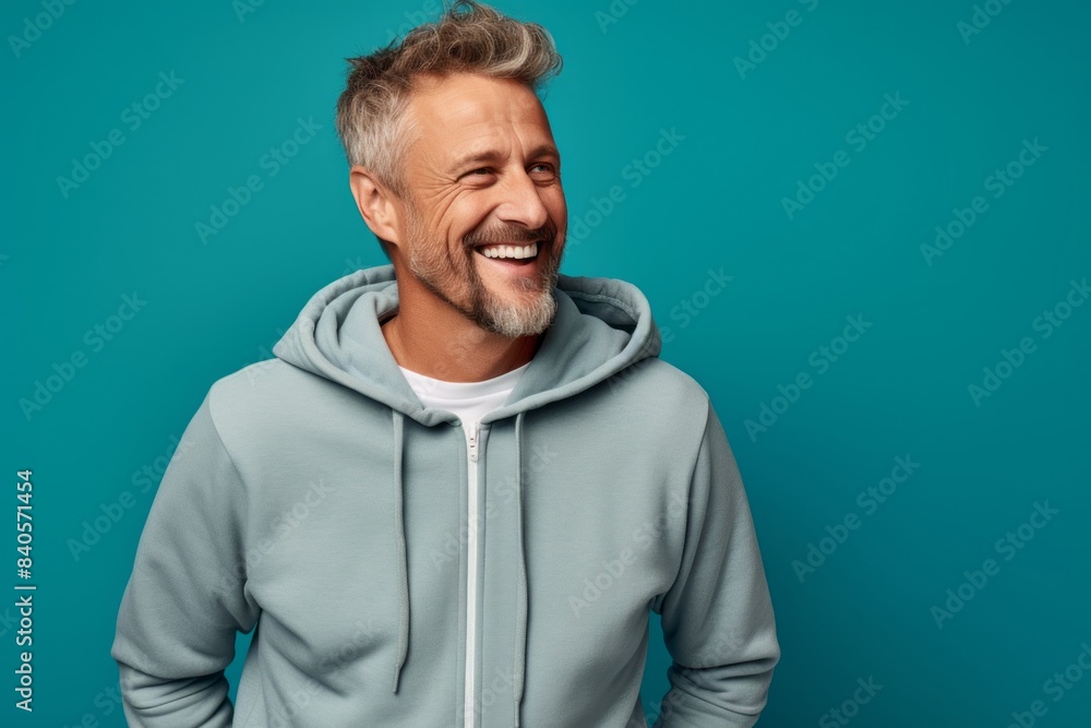 Portrait of a happy man in his 50s wearing a zip-up fleece hoodie in front of soft teal background Portrait of a happy man in his 50s wearing a zip-up fleece hoodie in front of soft teal background