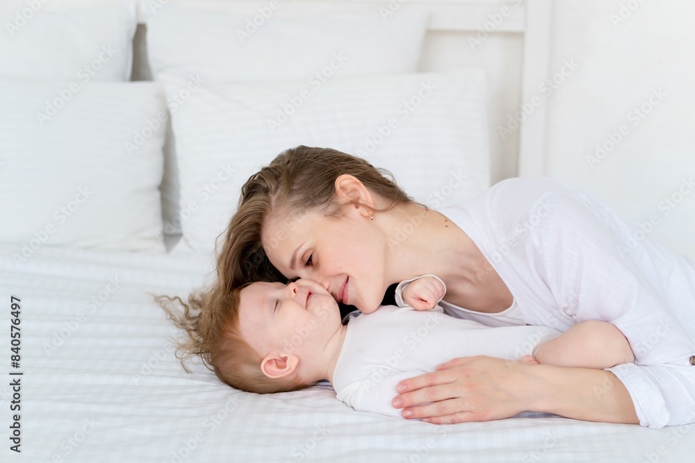a loving mother takes care of a newborn baby, mom and baby son gently hugs and kisses at home on the bed, maternal love and care, mom plays with the baby. portrait of a happy mother with a child, a loving mother takes care of a newborn baby, mom and baby son gently hugs and kisses at home on the bed, maternal love and care, mom plays with the baby. portrait of a happy mother with a child,