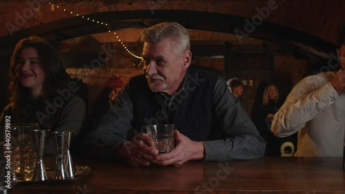 Three people drinks at the bar counter. Caucasian adult male enjoying a drink in restaurant. Addicted alcoholic order whiskey. Laughing man takes one more glass irish whisky.