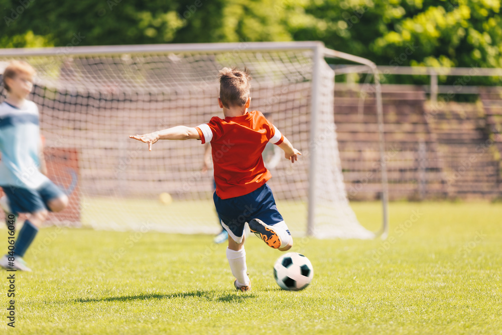 Obraz premium Little Boy Kick Soccer Ball During League Match. Happy Kid Have Fun Shooting Ball Towards Soccer Goal. School Soccer Tournament Game For Kids