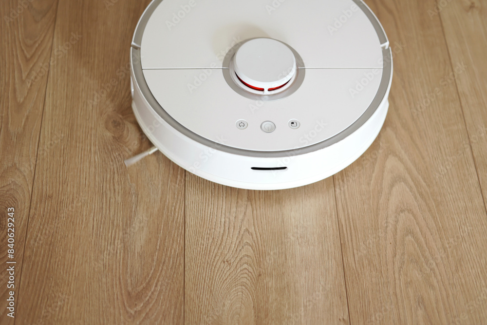 Top view of white wireless autonomous robotic vacuum cleaner on wooden floor. Smart cleaning technology. Self-propelled cleaning robot. Floor cleaning system. Household remote control appliances. Top view of white wireless autonomous robotic vacuum cleaner on wooden floor. Smart cleaning technology. Self-propelled cleaning robot. Floor cleaning system. Household remote control appliances.