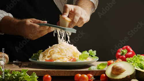 Fotografie Chef grates hard cheese on top of a freshly prepared pasta dish, Pasta is mediterranean Italian traditional cuisine