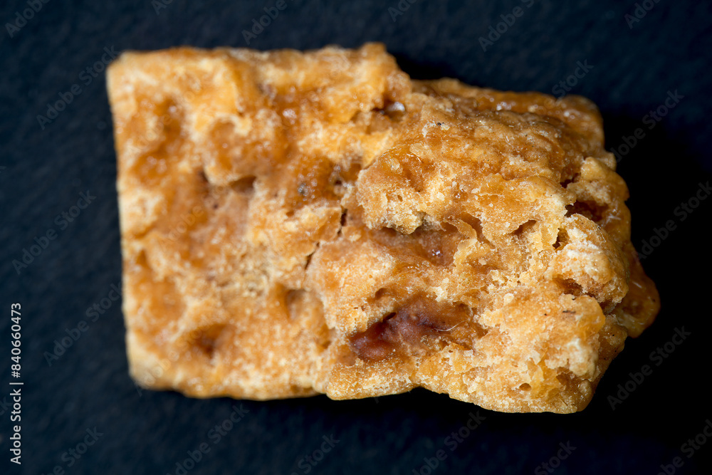 A close-up shot of a square of asafoetida, isolated against a black background. A close-up shot of a square of asafoetida, isolated against a black background.