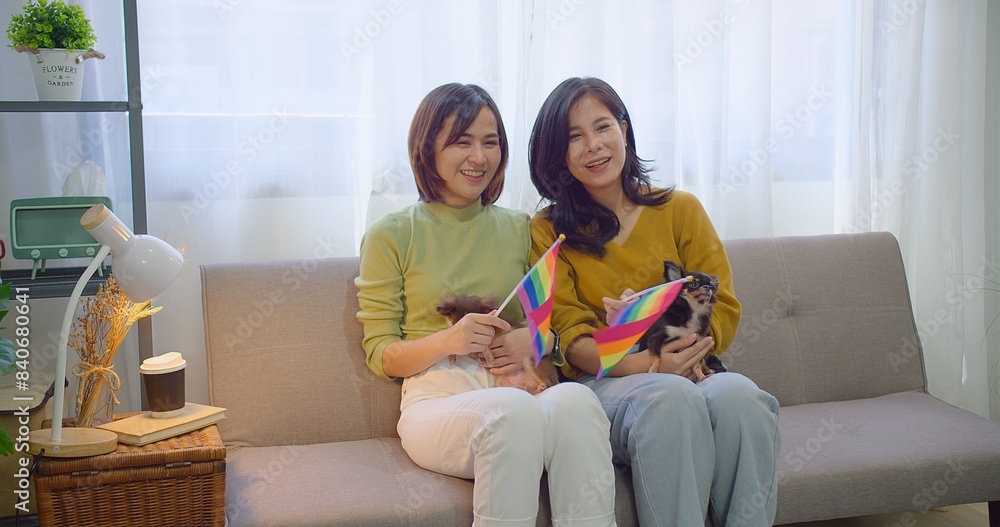 Two Asian women lesbian share a comforting tender moment smiles and a loving embrace on a sofa draped in a rainbow flag with two small dogs beside them in a cozy home Two Asian women lesbian share a comforting tender moment smiles and a loving embrace on a sofa draped in a rainbow flag with two small dogs beside them in a cozy home