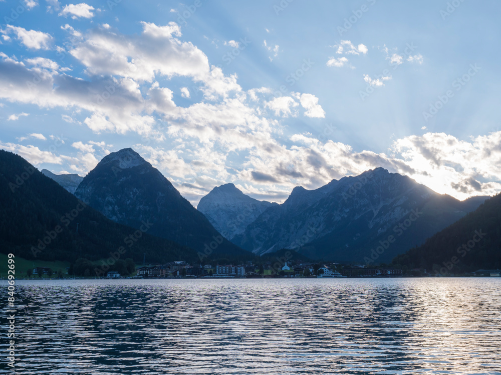 View of Pertisau village on shore of Achensee, Achen lake surrounded by Alps, Karwendel mountain range. View from the opposite site. Summer day during sunset, lense flare, backlight. Tyrol, Austria View of Pertisau village on shore of Achensee, Achen lake surrounded by Alps, Karwendel mountain range. View from the opposite site. Summer day during sunset, lense flare, backlight. Tyrol, Austria