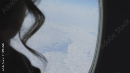 A woman admires clouds through the airplane window as she travels through the sky