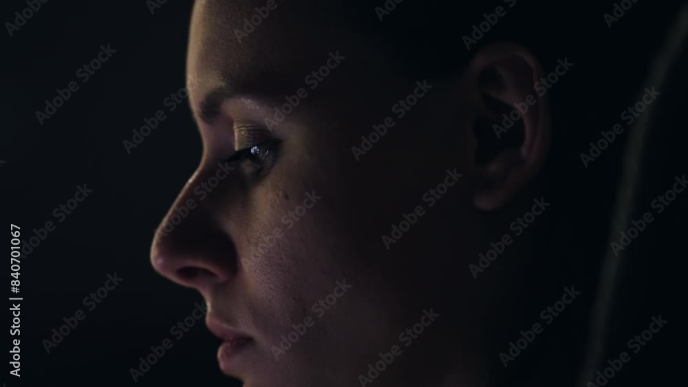 Woman look at flickering tv or phone with face partially illuminated in a dark setting, reflecting deep emotion or contemplation. Woman look at flickering tv or phone with face partially illuminated in a dark setting, reflecting deep emotion or contemplation.
