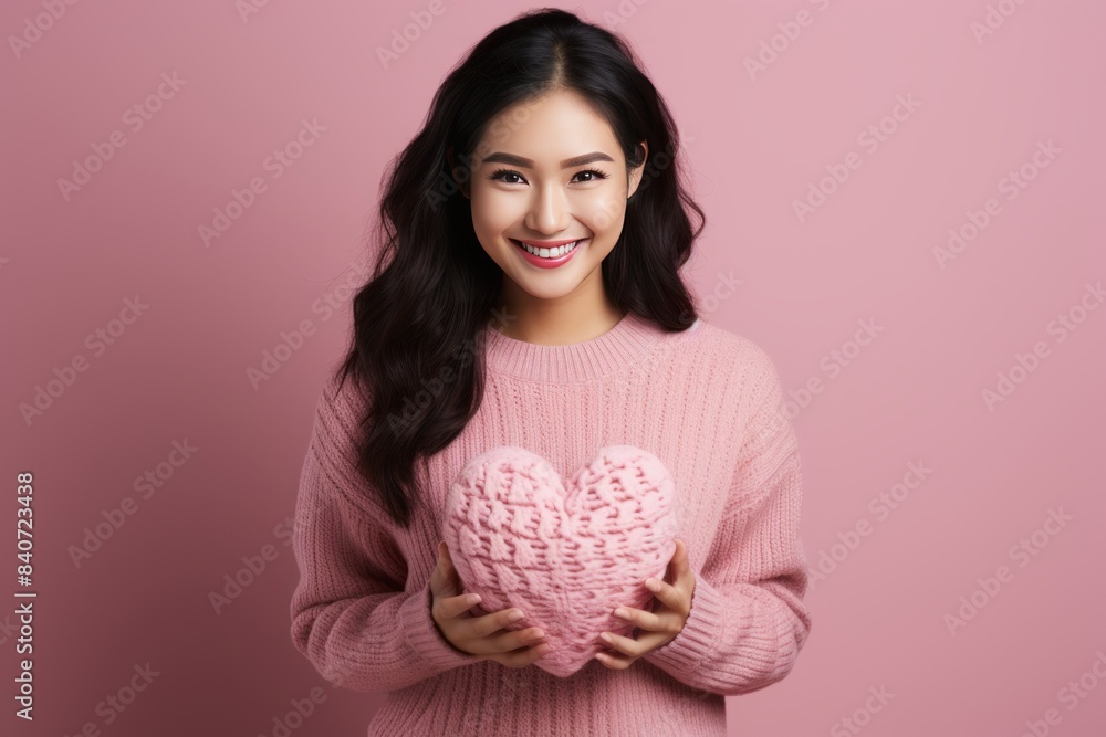 Young Asian woman in pink sweater holding a heart-shaped cushion Young Asian woman in pink sweater holding a heart-shaped cushion