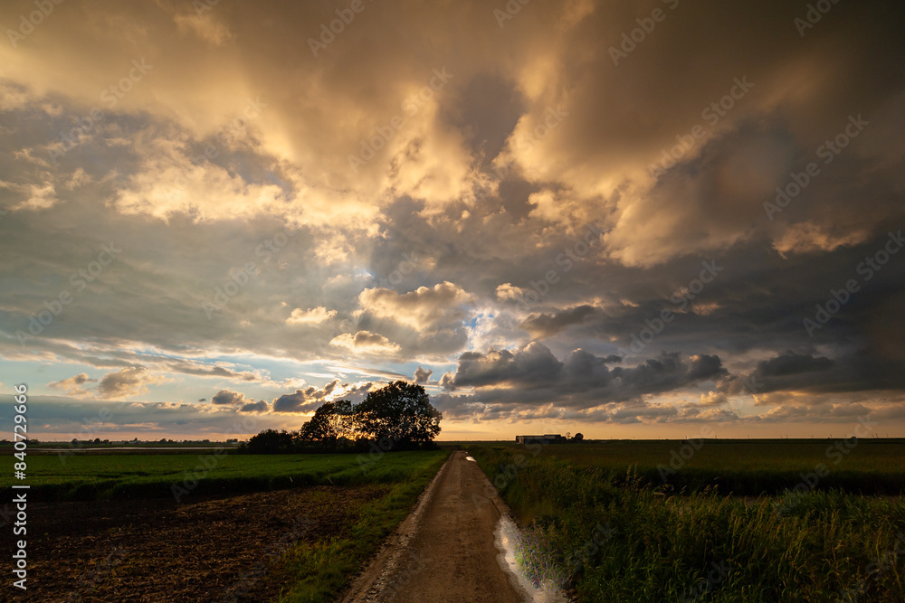 Fototapeta premium Dramatic landscape image of a colorful cloud sky over a country road after the passage of a rain shower
