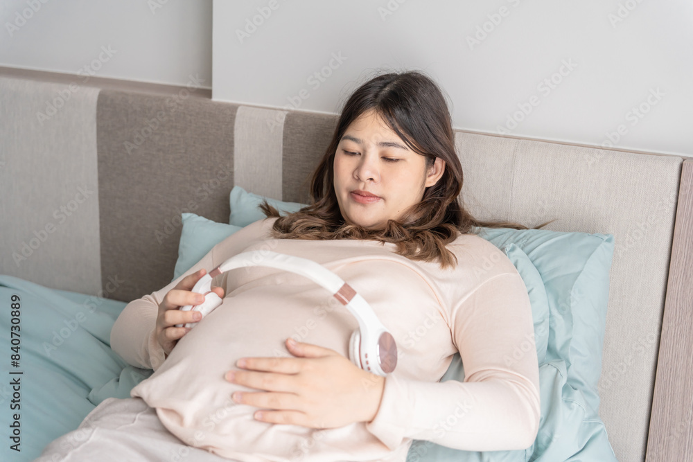 Pregnant asian woman holding headphone on belly playing music to her baby in stomach relaxing pregnancy Mental health concept Pregnant asian woman holding headphone on belly playing music to her baby in stomach relaxing pregnancy Mental health concept