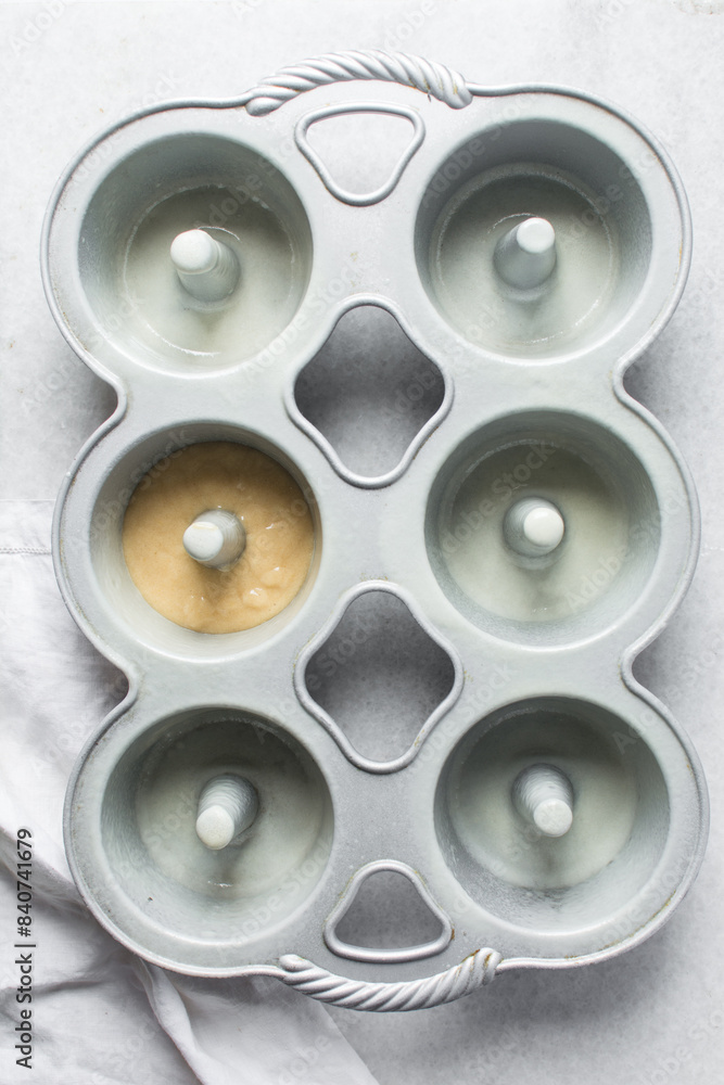 Overhead view of vanilla cake batter in mini bundt cake pan, top view of cake batter in silver bundtlette baking pans, process of making mini bundt cakes Overhead view of vanilla cake batter in mini bundt cake pan, top view of cake batter in silver bundtlette baking pans, process of making mini bundt cakes
