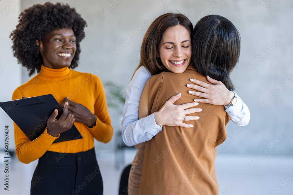 A joyful group of diverse businesswomen engages in a supportive embrace in a modern office setting, with one holding a clipboard, dressed in professional attire. A joyful group of diverse businesswomen engages in a supportive embrace in a modern office setting, with one holding a clipboard, dressed in professional attire.