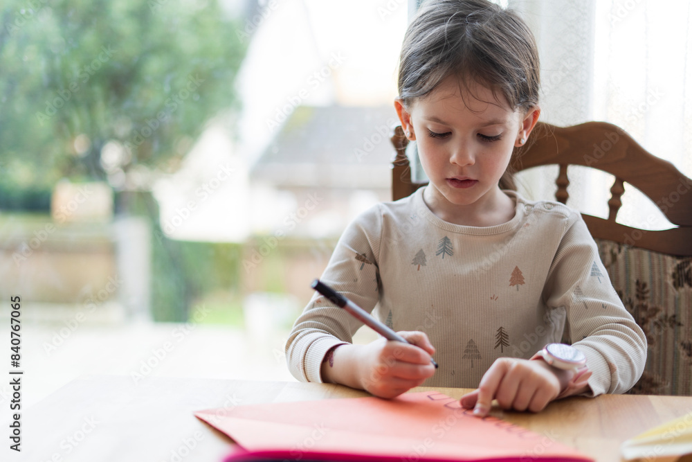 A little cute girl with a ponytail, sitting at a living room table, does her homework, holding a pen in her hand. Home education concept. A little cute girl with a ponytail, sitting at a living room table, does her homework, holding a pen in her hand. Home education concept.