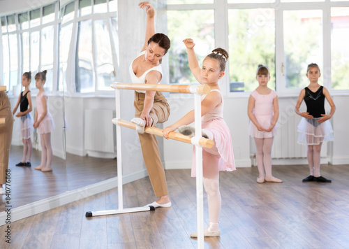 Little ballerinas together with choreography teacher in the grand batman pose learn to dance ballet