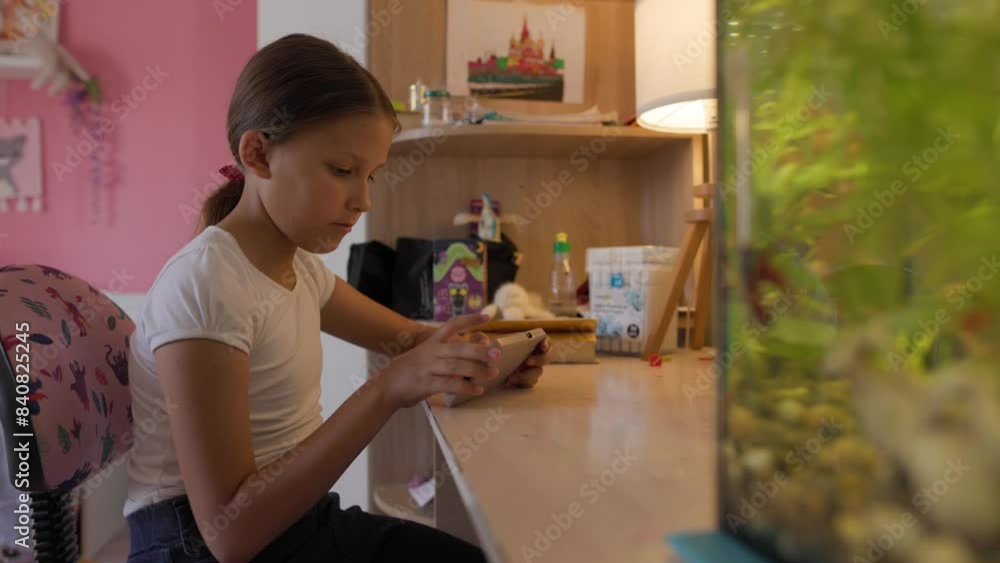 A girl sits at a table with an aquarium with fish and uses a smartphone A girl sits at a table with an aquarium with fish and uses a smartphone