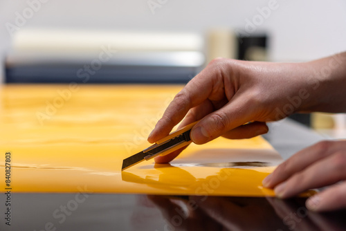 Fotografie Close-up of a man's hand working with a knife and cutting self-adhesive film to make a sticker