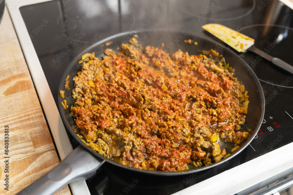 Minced meat with tomato sauce is fried in a frying pan in the kitchen. Homemade food concept. Minced meat with tomato sauce is fried in a frying pan in the kitchen. Homemade food concept.