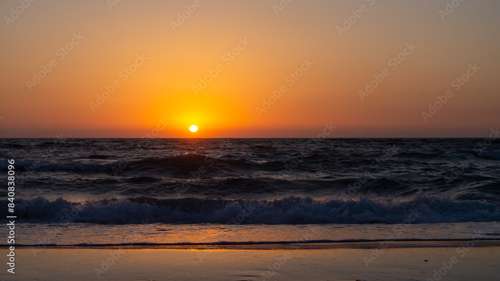 Beautiful sunset over a sandy beach with the sun setting into the sea. Golden light reflects off the calm waves, creating a serene and picturesque coastal scene perfect for relaxation and nature-theme Beautiful sunset over a sandy beach with the sun setting into the sea. Golden light reflects off the calm waves, creating a serene and picturesque coastal scene perfect for relaxation and nature-theme