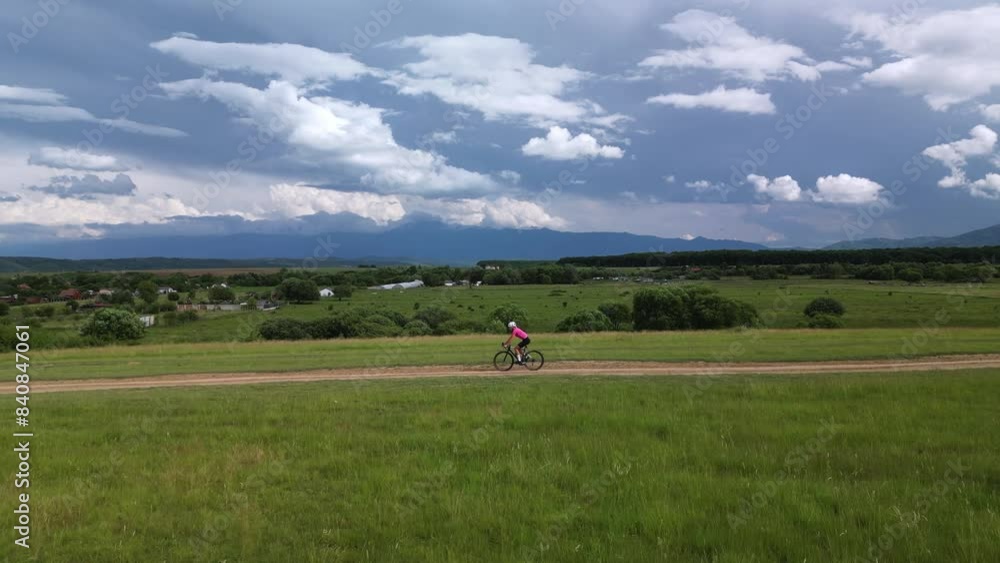 Aerial drone view of woman cyclist on gravel bike riding across the green field on gravel road.Beautiful and inspiring off road cycling destination. Cycling in mountains.Sport mood motivational video. Aerial drone view of woman cyclist on gravel bike riding across the green field on gravel road.Beautiful and inspiring off road cycling destination. Cycling in mountains.Sport mood motivational video.