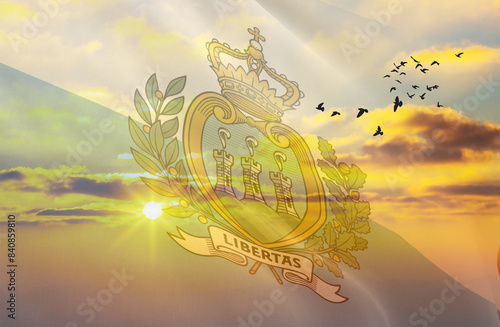 Waving the flag of San Marino against the background of a sunset or sunrise. San Marino flag for Independence Day. The symbol of the state on wavy fabric.