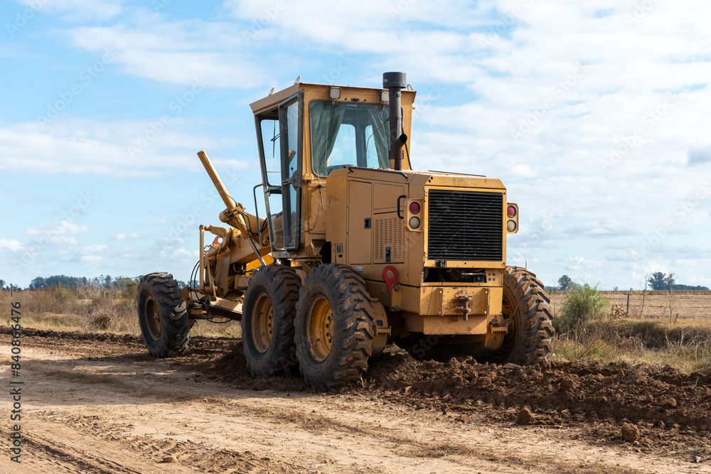 Heavy machinery is working on a dirt road in a rural setting under a partly cloudy sky. The image showcases two yellow graders and a green tractor, emphasizing construction and agricultural themes Heavy machinery is working on a dirt road in a rural setting under a partly cloudy sky. The image showcases two yellow graders and a green tractor, emphasizing construction and agricultural themes