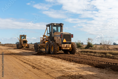Maquinaria pesada niveladora trabajando en la construcción de una carretera de tierra bajo un cielo despejado
