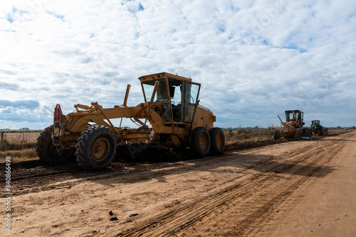 Maquinaria pesada niveladora trabajando en la construcción de una carretera de tierra bajo un cielo despejado