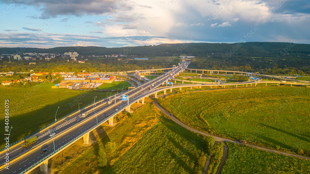 Fototapeta premium Warm sunset hues blanket the sky over the Lahovice Bridge and junction in Prague, with the intricate network of roads bustling with evening traffic.