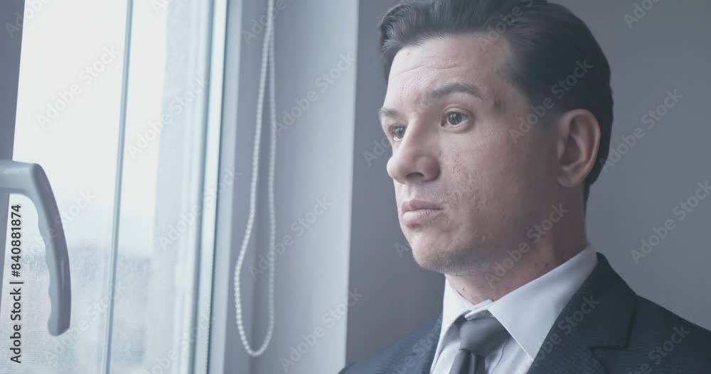 Close-up portrait of a sad young adult Caucasian man in a business suit and tie near the window Close-up portrait of a sad young adult Caucasian man in a business suit and tie near the window