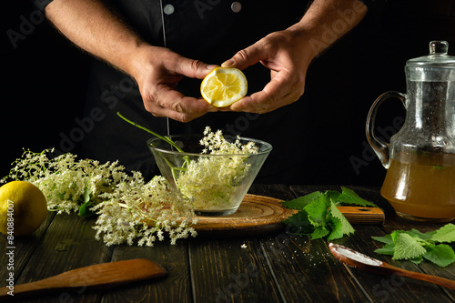 Cooking healthy kvass from elderflowers and lemon on the kitchen table by the hands of a cook. Refreshing and healing drink with mint and elderberry