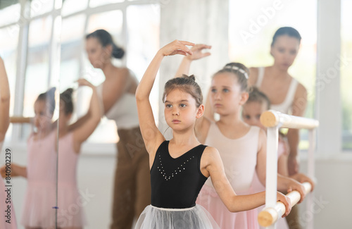 Group of ballerinas preparing for performance, learning and improving quality of rendering stage. Ballerinas near ballet bare repeat third position with supervision experienced female mentor © JackF