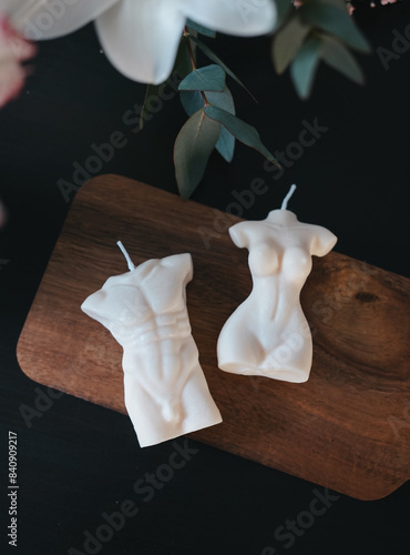 These unique candles, shaped like a man's torso and a woman's figure, are beautifully displayed on a wooden board, enhancing any decor with their artistic presence