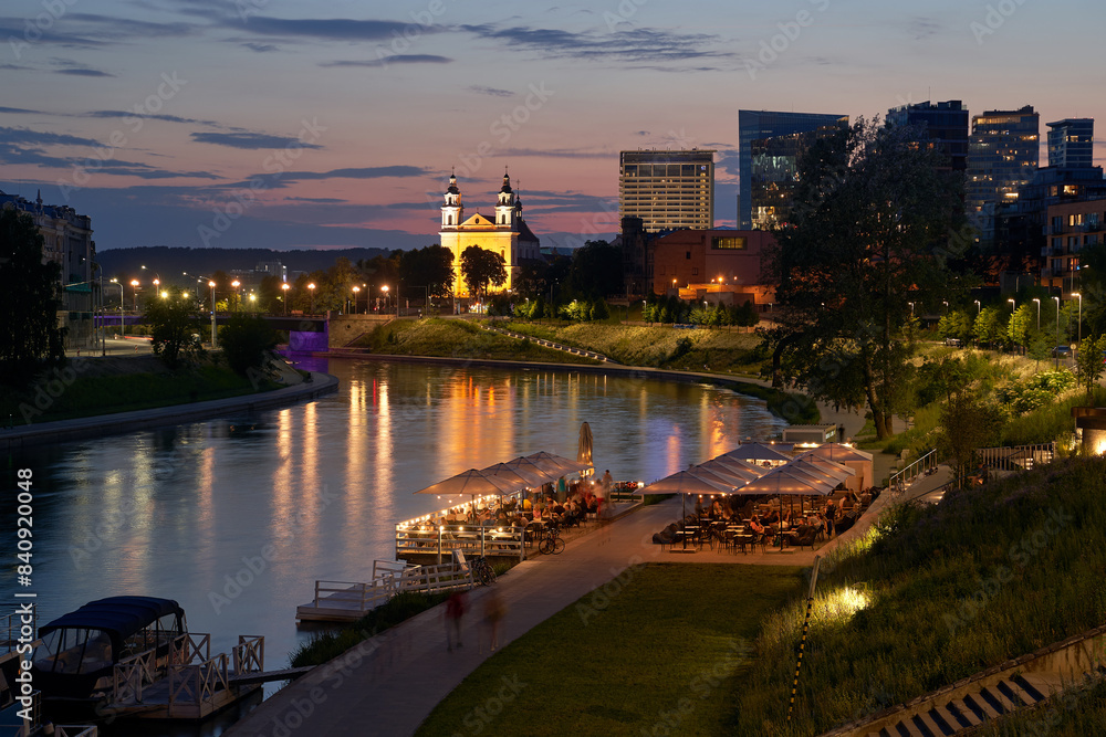 Vilnius night sunset panoramic cityscape with Neris river, boats, cafe, church and skyscrapers of New Center. Lithuania, Baltic states.