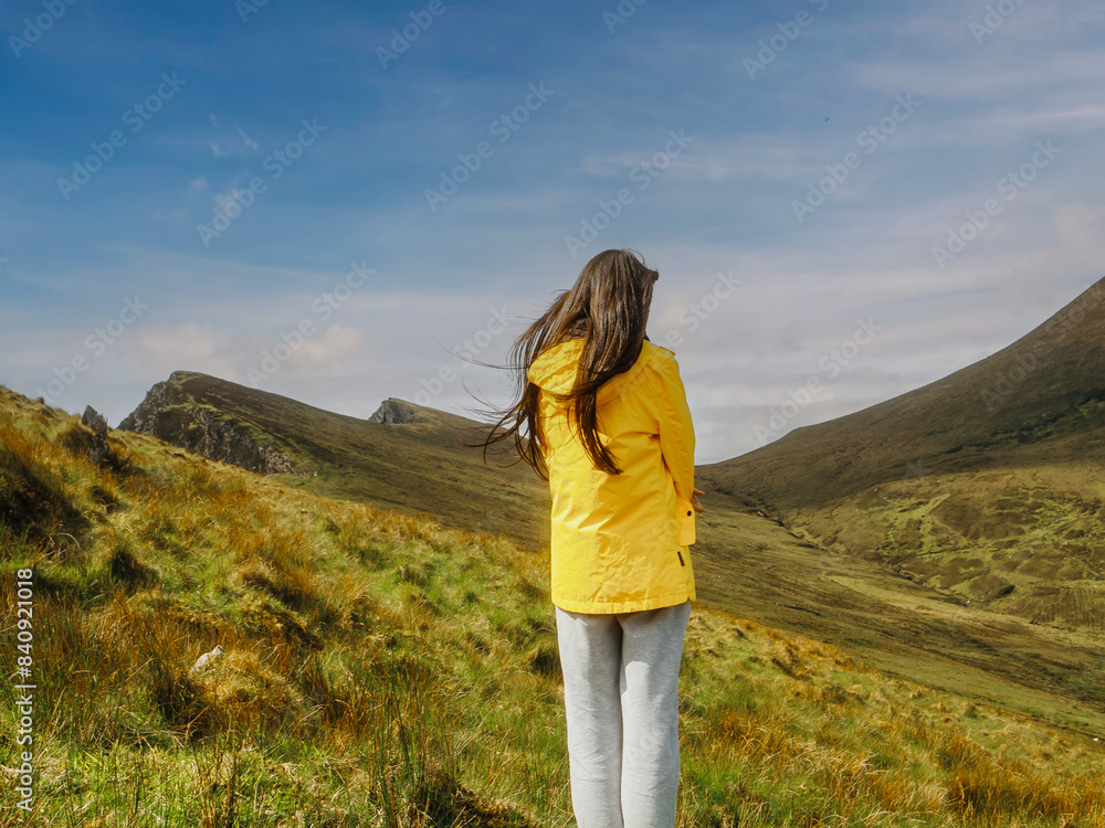 A teenager girl is standing on a grassy hill, looking out at the mountains in the distance. The scene is peaceful and serene, with the woman's gaze focused on the horizon. Travel in nature concept. A teenager girl is standing on a grassy hill, looking out at the mountains in the distance. The scene is peaceful and serene, with the woman's gaze focused on the horizon. Travel in nature concept.