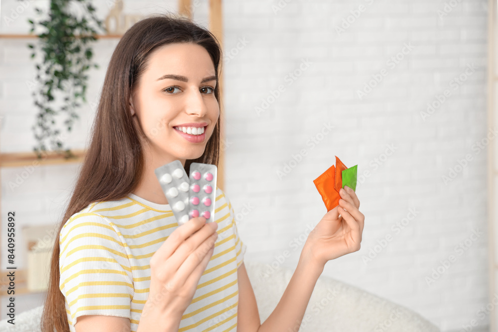 Beautiful young woman with birth control pills and condoms in living room Beautiful young woman with birth control pills and condoms in living room