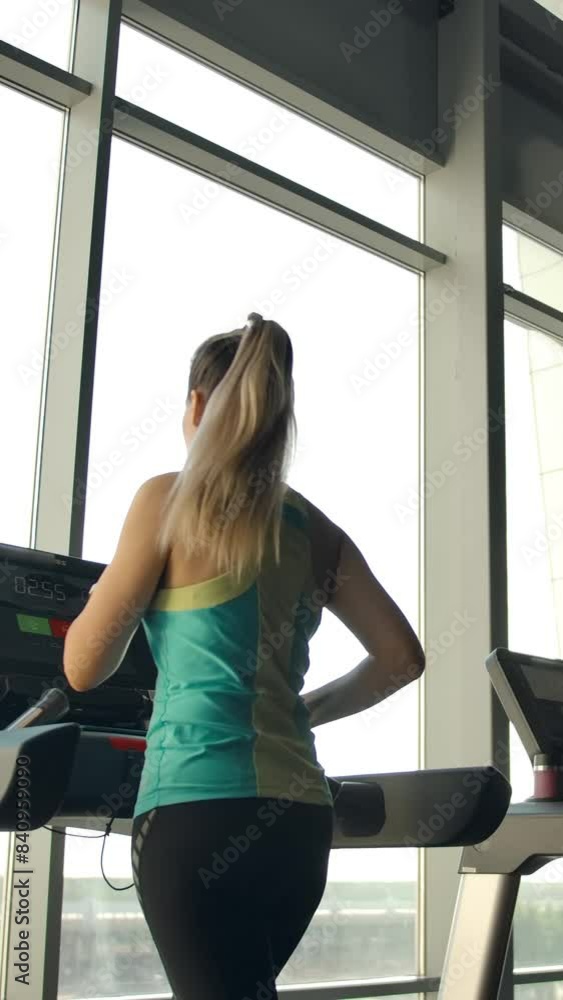 Athletes in the gym is engaged on treadmills. They walk at a calm pace looking through the large windows in a modern gym. Vertical shot. Athletes in the gym is engaged on treadmills. They walk at a calm pace looking through the large windows in a modern gym. Vertical shot.