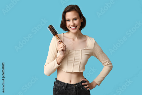 Beautiful young happy woman with bob hairstyle holding brush on blue background