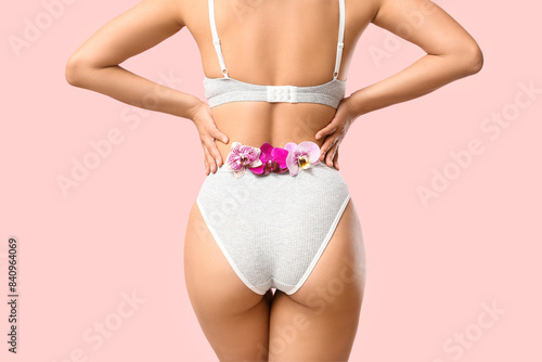 Young woman in underwear with beautiful orchid flowers on pink background  back view