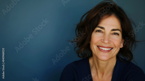 Closeup portrait of mid aged professional businesswoman, beautiful confident adult woman in navy top smiling isolated on blue background