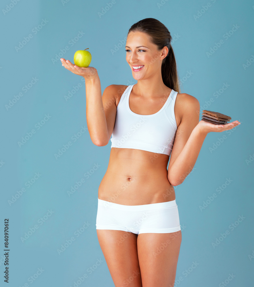 Smile, woman and chocolate with apple food choice isolated on studio, sugar and diet in blue background. Dessert, young vegetarian person for detox and green fruit, lose weight decision or vegan Smile, woman and chocolate with apple food choice isolated on studio, sugar and diet in blue background. Dessert, young vegetarian person for detox and green fruit, lose weight decision or vegan
