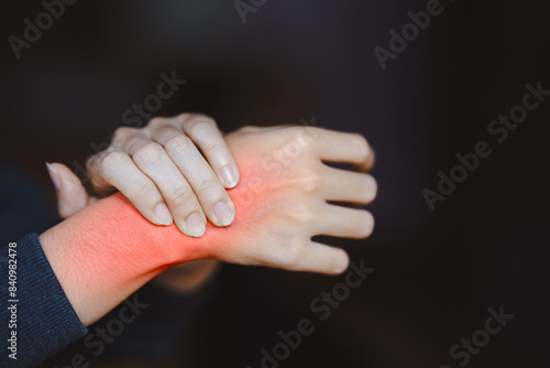 Obraz na plátně Close-up of person in black sleeve pressing red-lit wrist representing pain, discomfort, or injury on dark background