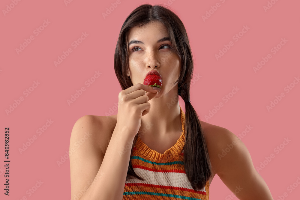 Beautiful young woman eating fresh strawberry on pink background Beautiful young woman eating fresh strawberry on pink background